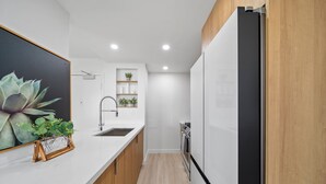 Eine moderne Küche mit weißen Arbeitsplatten, Holzschränken, einem eingebauten Backofen und einem schwarzen Kühlschrank.