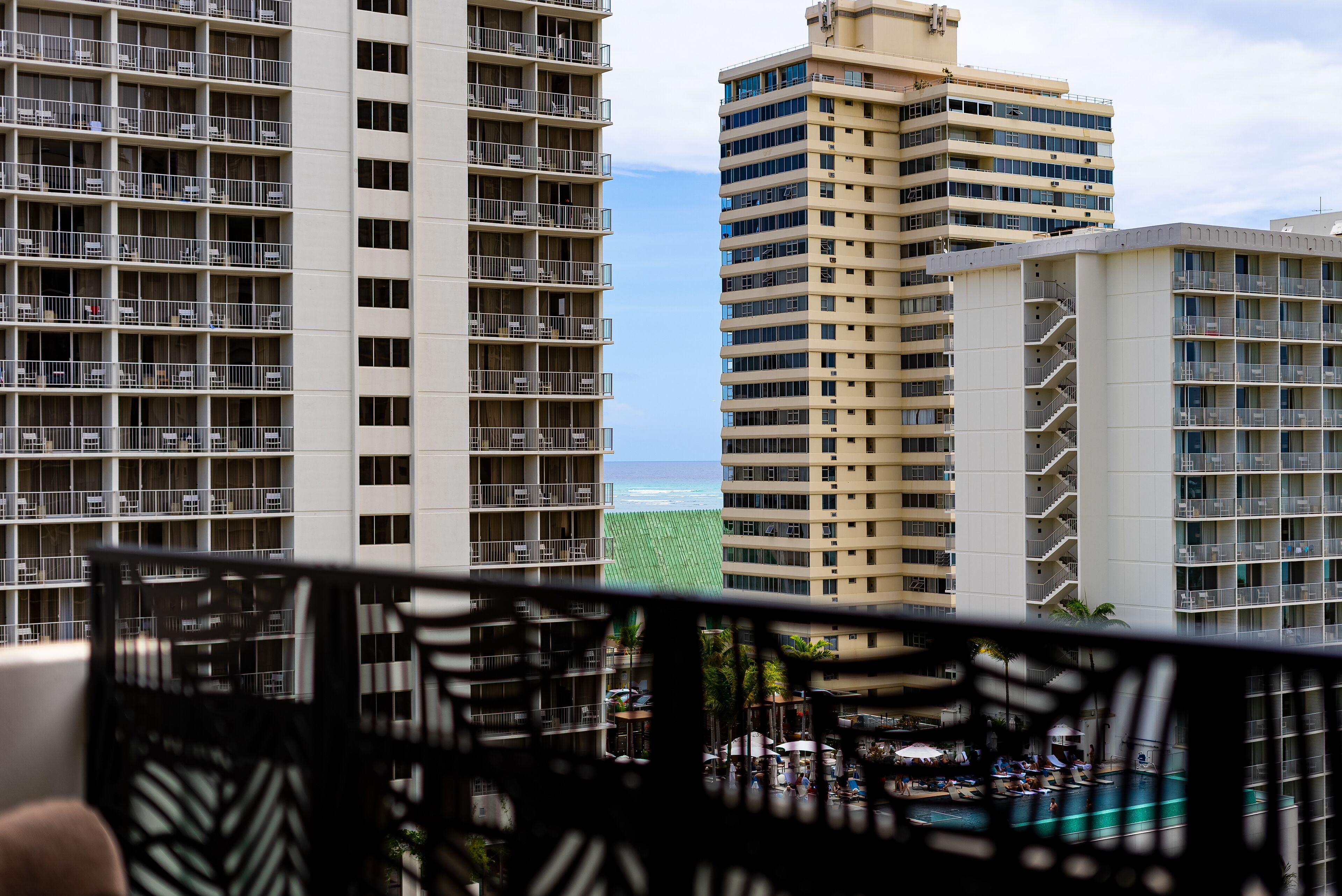 A high-rise hotel with multiple balconies, a pool area, and a view of the ocean.