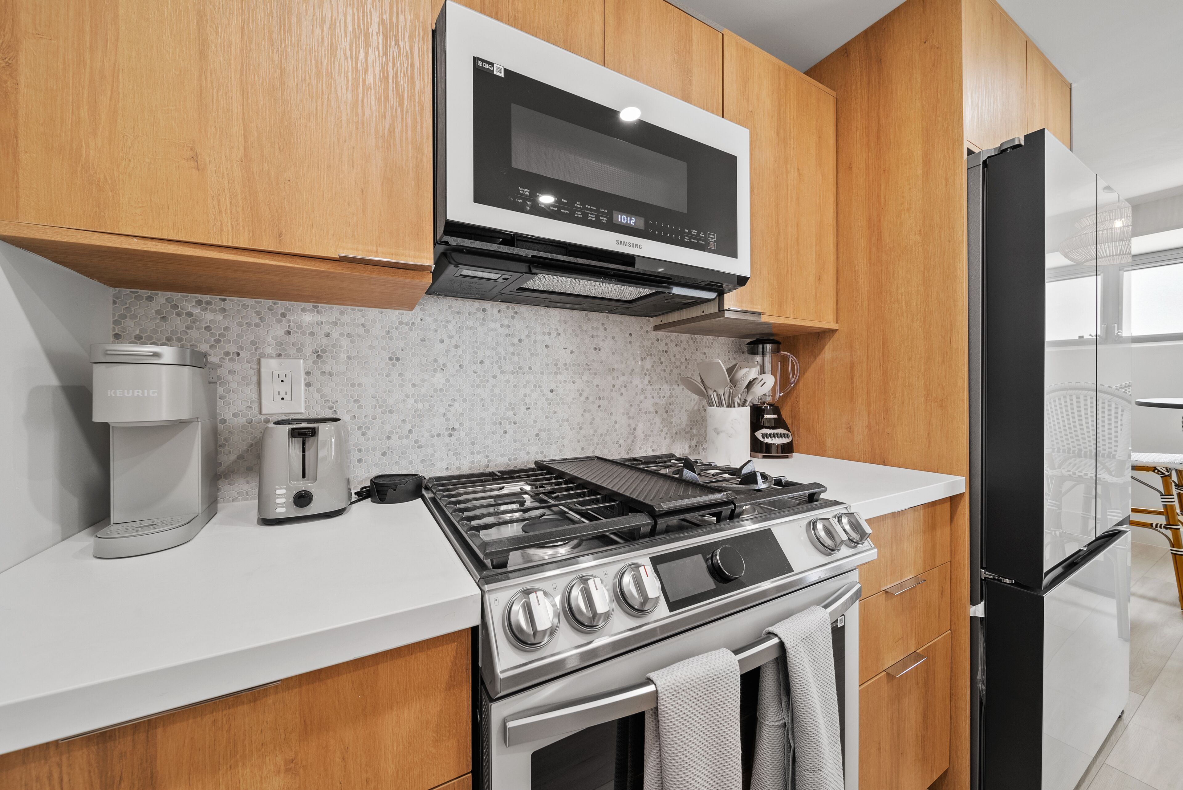 A modern kitchen with wooden cabinets, a built-in microwave, a gas stove, and a black refrigerator.
