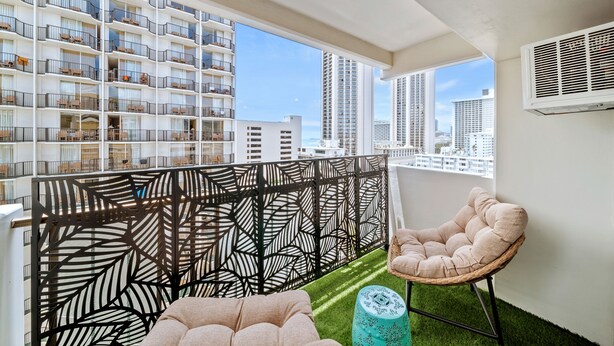 Ein Balkon mit einem dekorativen, schwarzen Metallzaun, einem gepolsterten Stuhl und einem kleinen, runden Hocker.