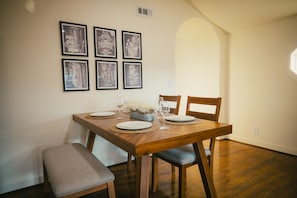 Un coin repas avec une table en bois, dressée pour quatre personnes, entourée de chaises, et des tableaux encadrés accrochés au mur.