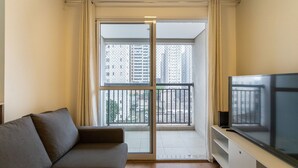 A living room with a sofa, a TV on a stand, and a balcony with a city view. - Capital Brás - Negócios e Lazer (São Paulo)