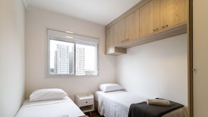 A small, well-lit room with two beds, a window with a city view, and a wooden cabinet above the beds. - Capital Brás - Negócios e Lazer (São Paulo)