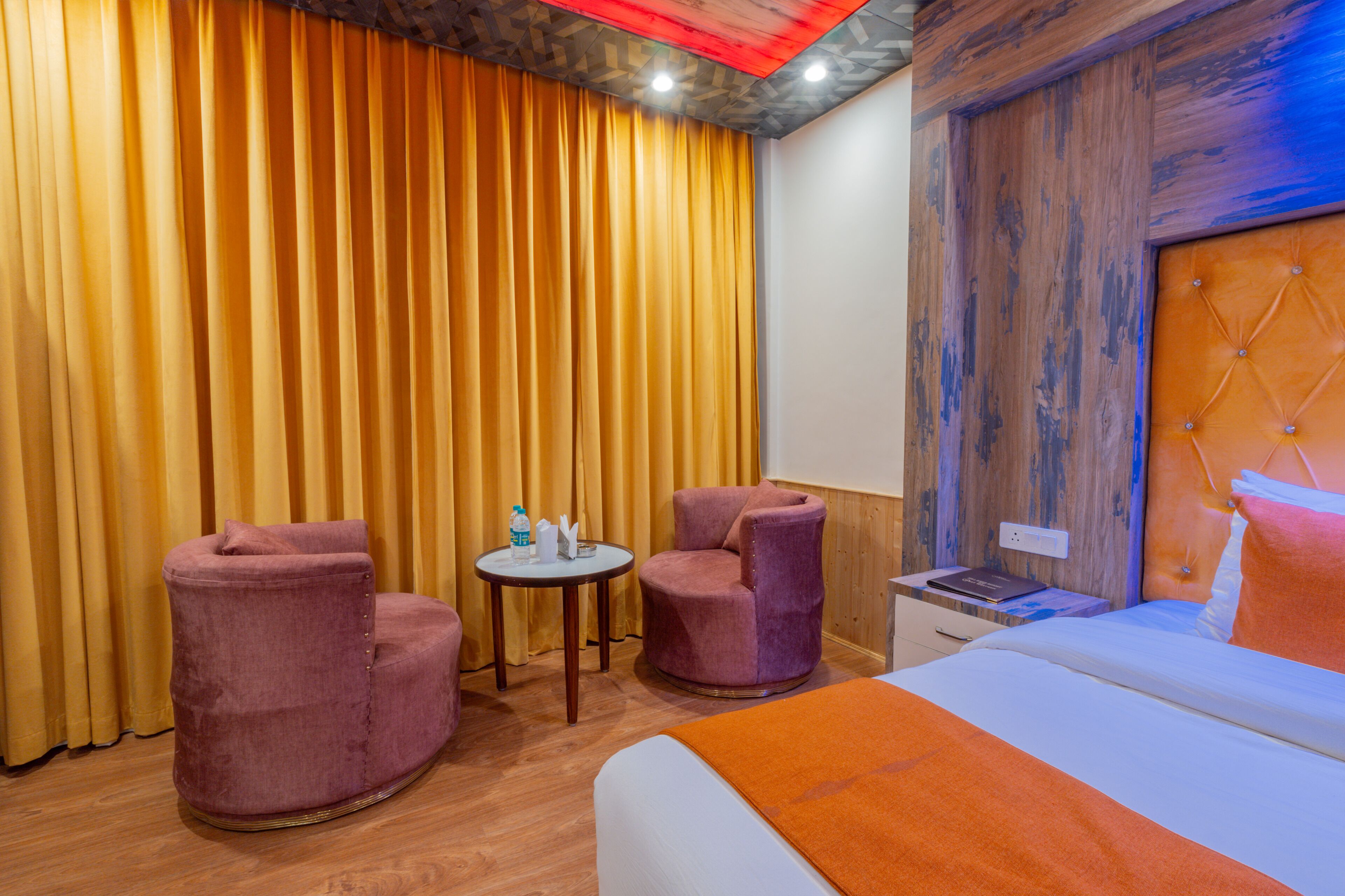 A hotel room with a bed, two armchairs, a small table, and a wooden headboard.