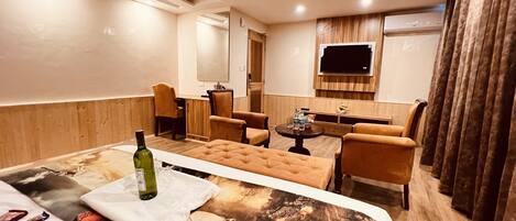 A hotel room with a large bed, a small table, two armchairs, a TV, and a wooden panel wall.