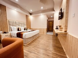 Habitación de hotel moderna con una cama grande, televisor montado en la pared, piso de madera y una pequeña zona de estar.