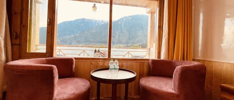 A room with two plush armchairs, a small round table, and a large window offering a mountain view.