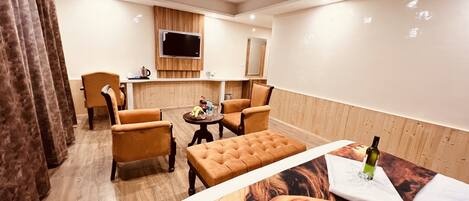 A hotel room with a wooden floor, a large bed, a TV, a small table with a bottle, and two chairs.