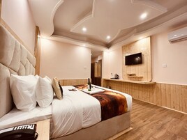 Una habitación de hotel moderna con una cama grande, un televisor de pantalla plana montado en la pared y suelo de madera.