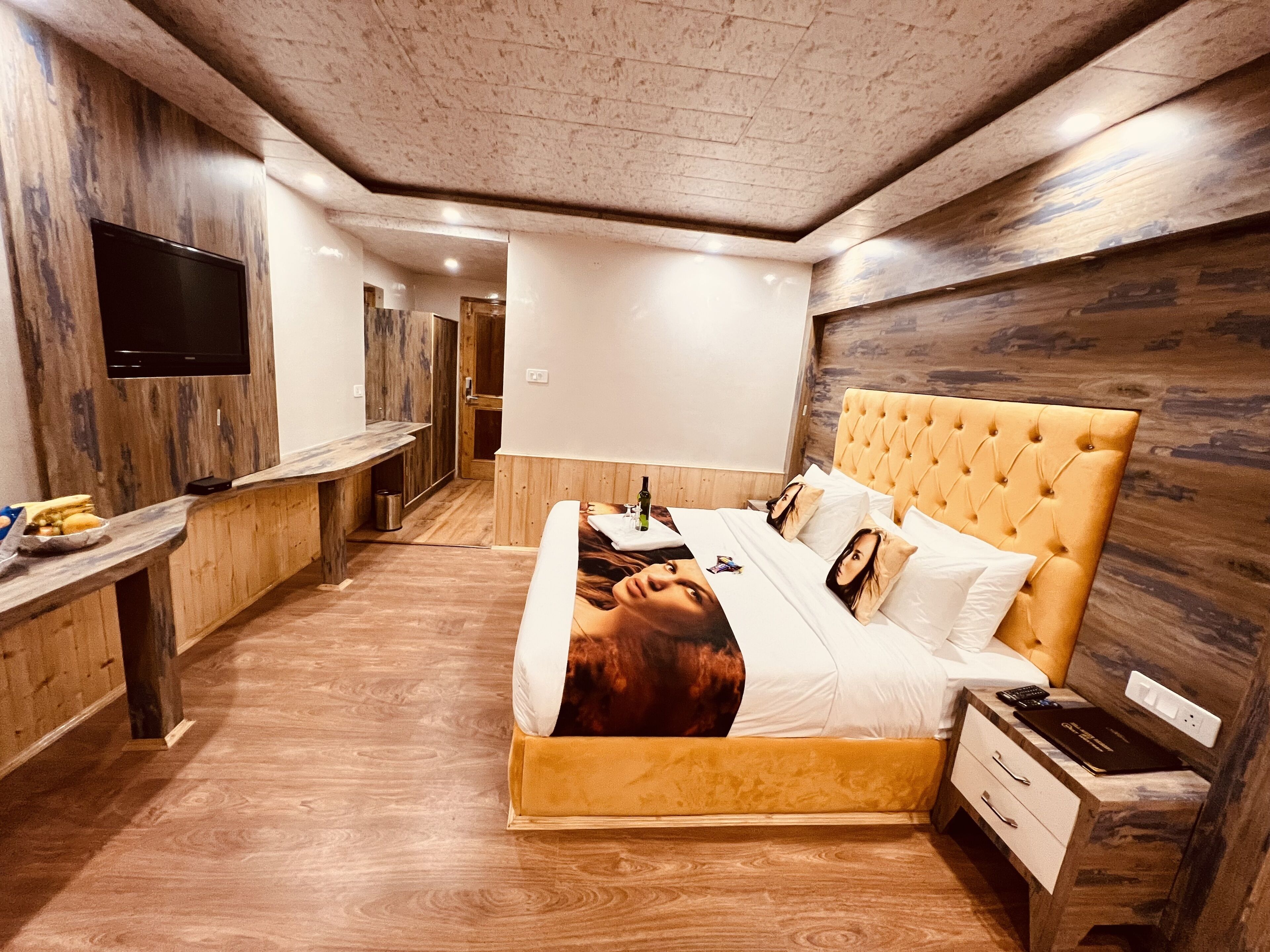 Un dormitorio moderno con cabecera de madera, televisor de pantalla plana en la pared, mesita de noche con lámpara y armario empotrado.