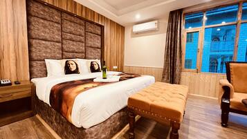 Een slaapkamer met een groot bed, een houten hoofdbord, een nachtkastje met een telefoon en een raam met uitzicht op een blauw gebouw.