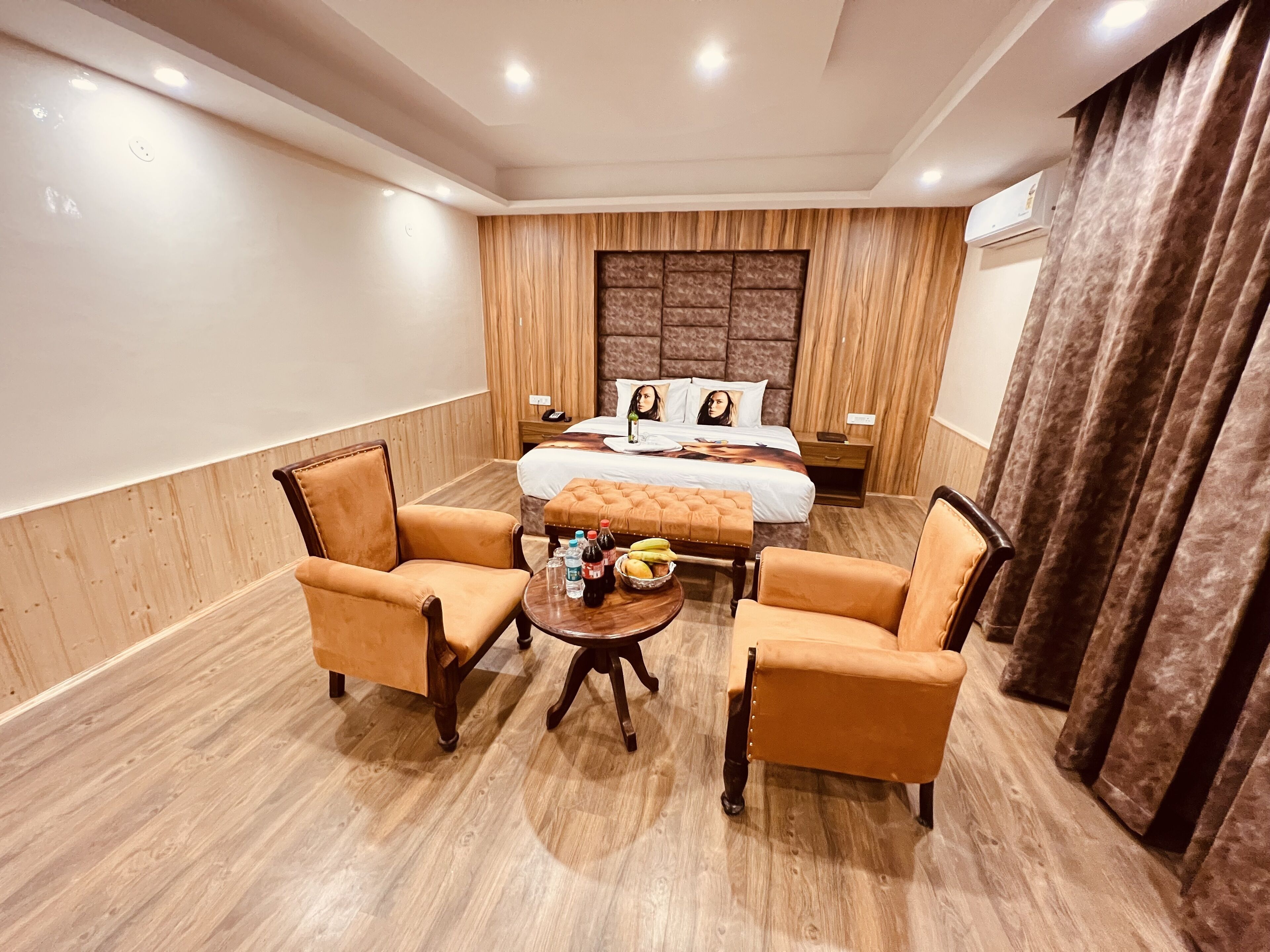 A hotel room with a large bed, two armchairs, a coffee table, and a wooden floor.