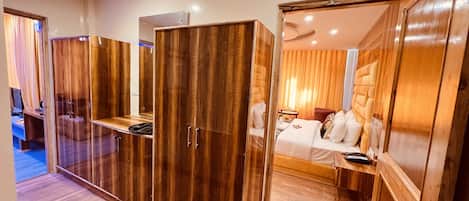 A hotel room with a wooden wardrobe, a bed, a desk, and a mirror.