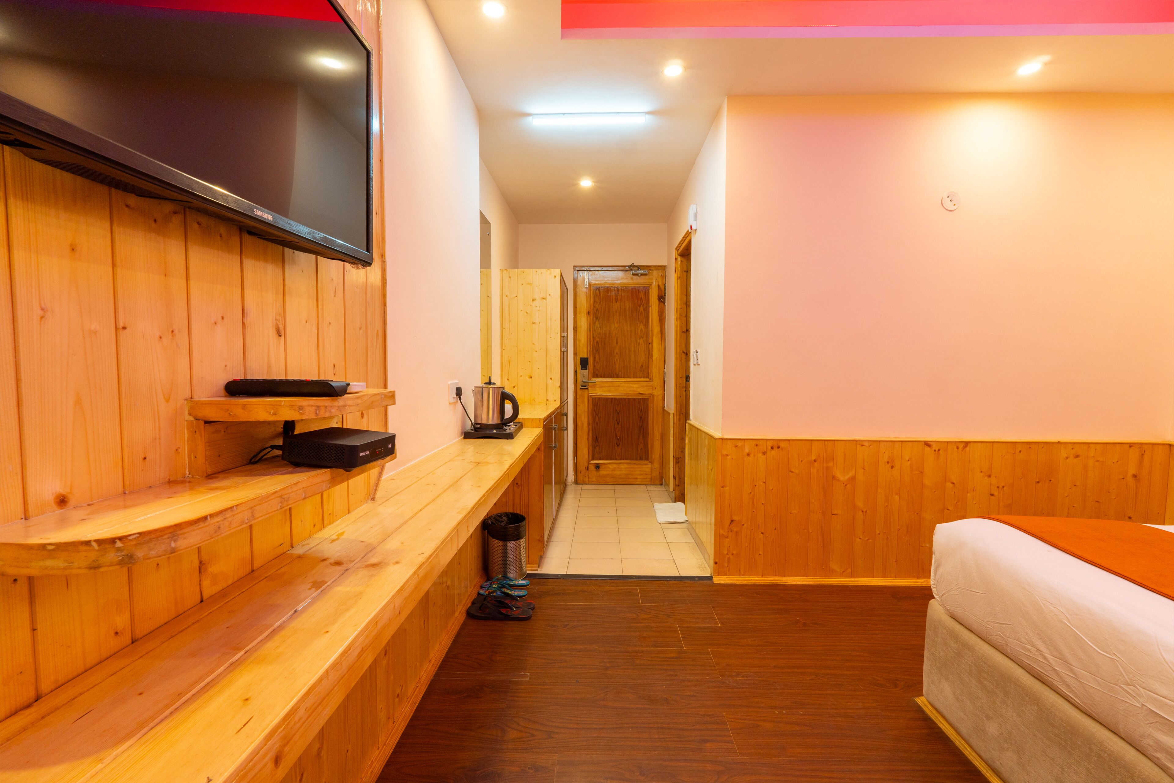 Une chambre d’hôtel avec un banc en bois, un téléviseur à écran plat, un lit et une porte en bois.