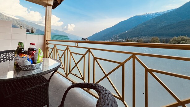 Un balcón con vistas a un lago y montañas, una mesa con bebidas embotelladas y una silla de mimbre.