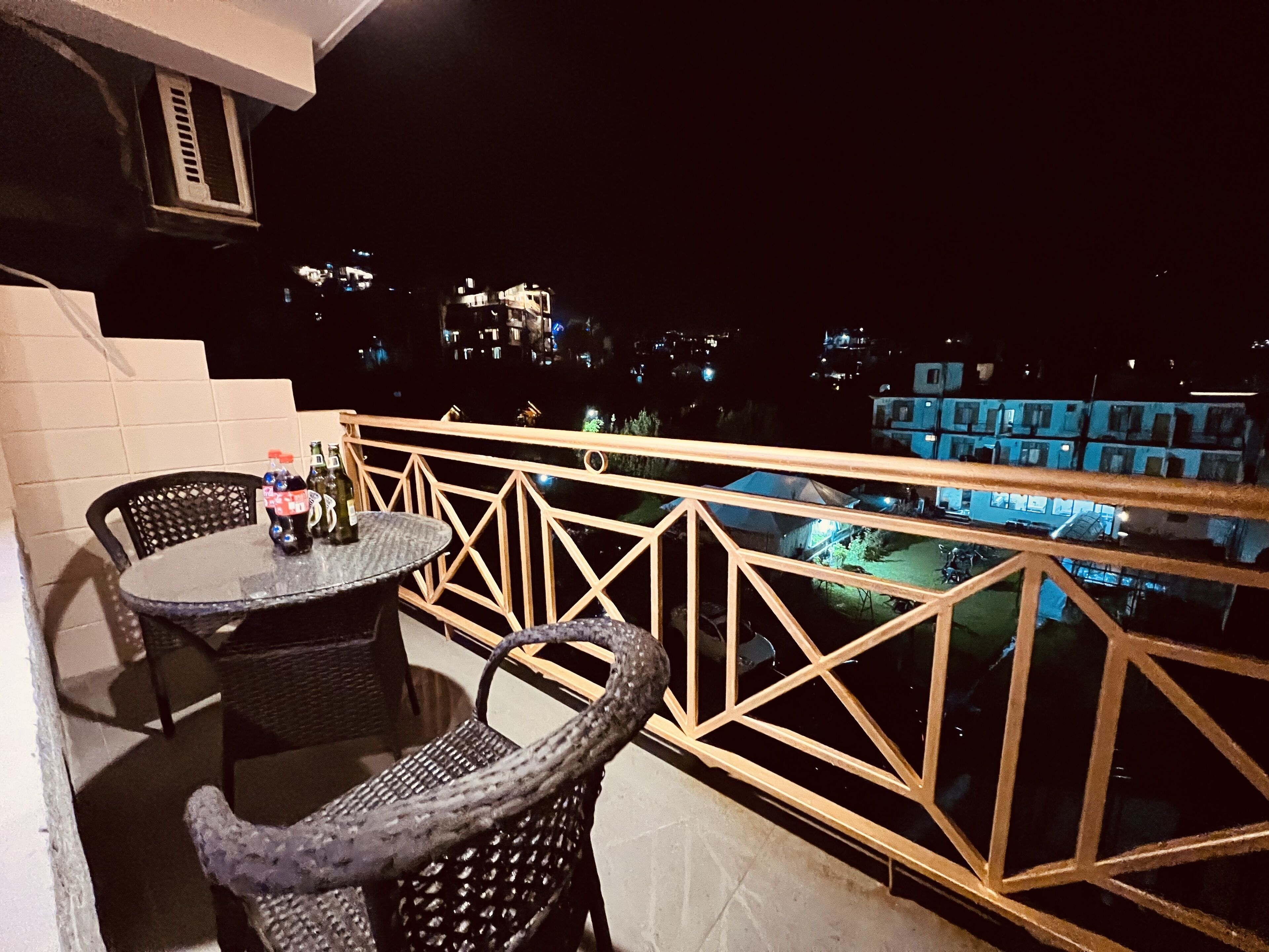 A balcony with a table and chairs, overlooking a residential area at night.