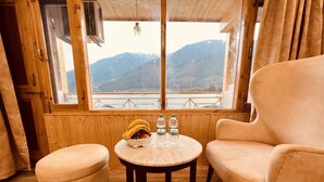 Una habitación acogedora con detalles de madera, una mesa redonda con cojín, una silla y una ventana con vistas a la montaña.