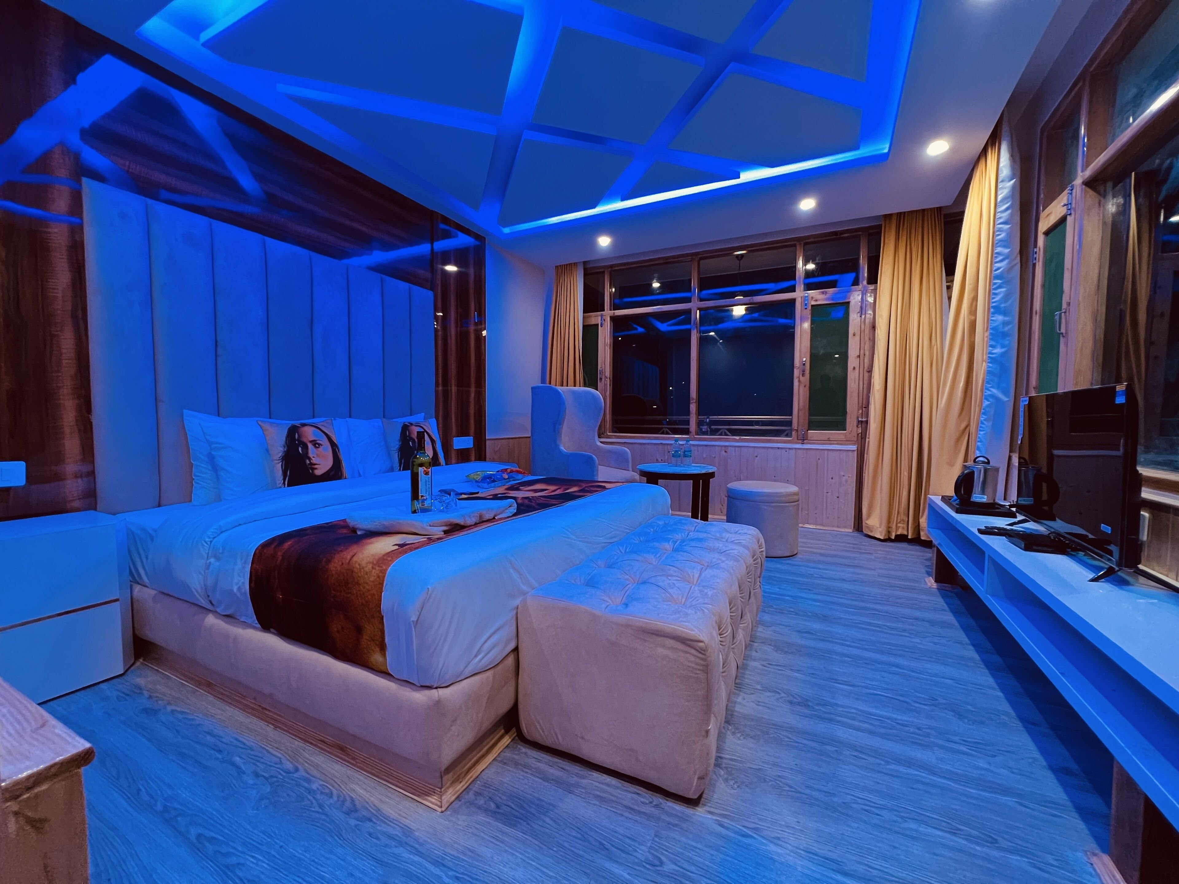 Une chambre d’hôtel moderne avec un grand lit, un coin salon équipé d’une télévision et une fenêtre avec des rideaux.