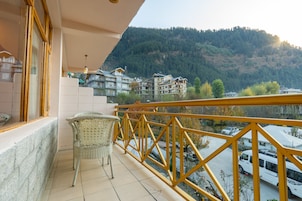 A balcony with a wicker chair, a yellow railing, and a view of buildings and a forested hill.