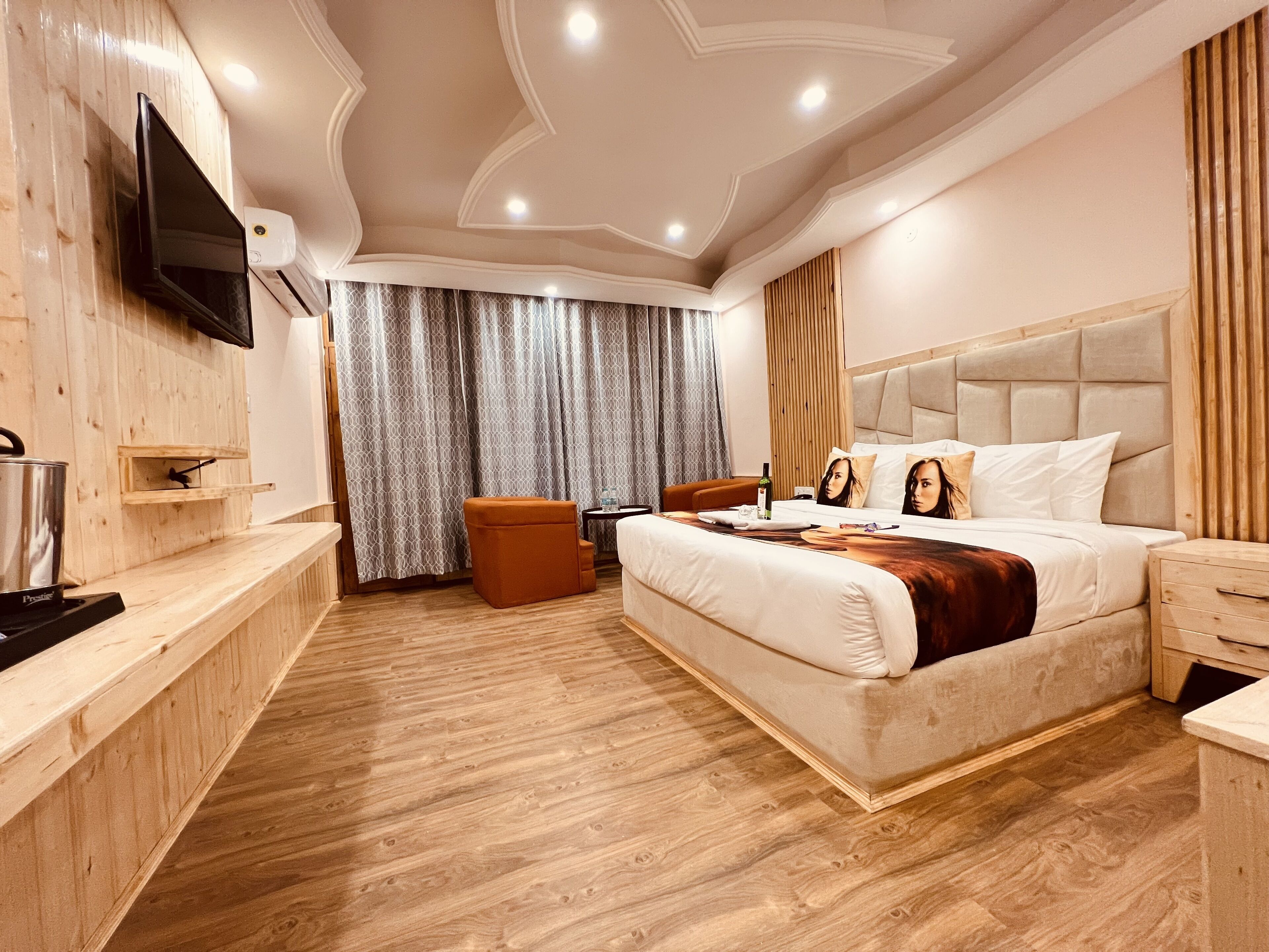 Een moderne hotelkamer met een houten vloer, een bed met hoofdeinde, een aan de muur bevestigde televisie en een klein tafeltje met stoel.