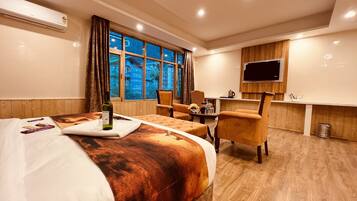 A hotel room with a bed, two armchairs, a small table, a TV, and a window with a view of buildings.