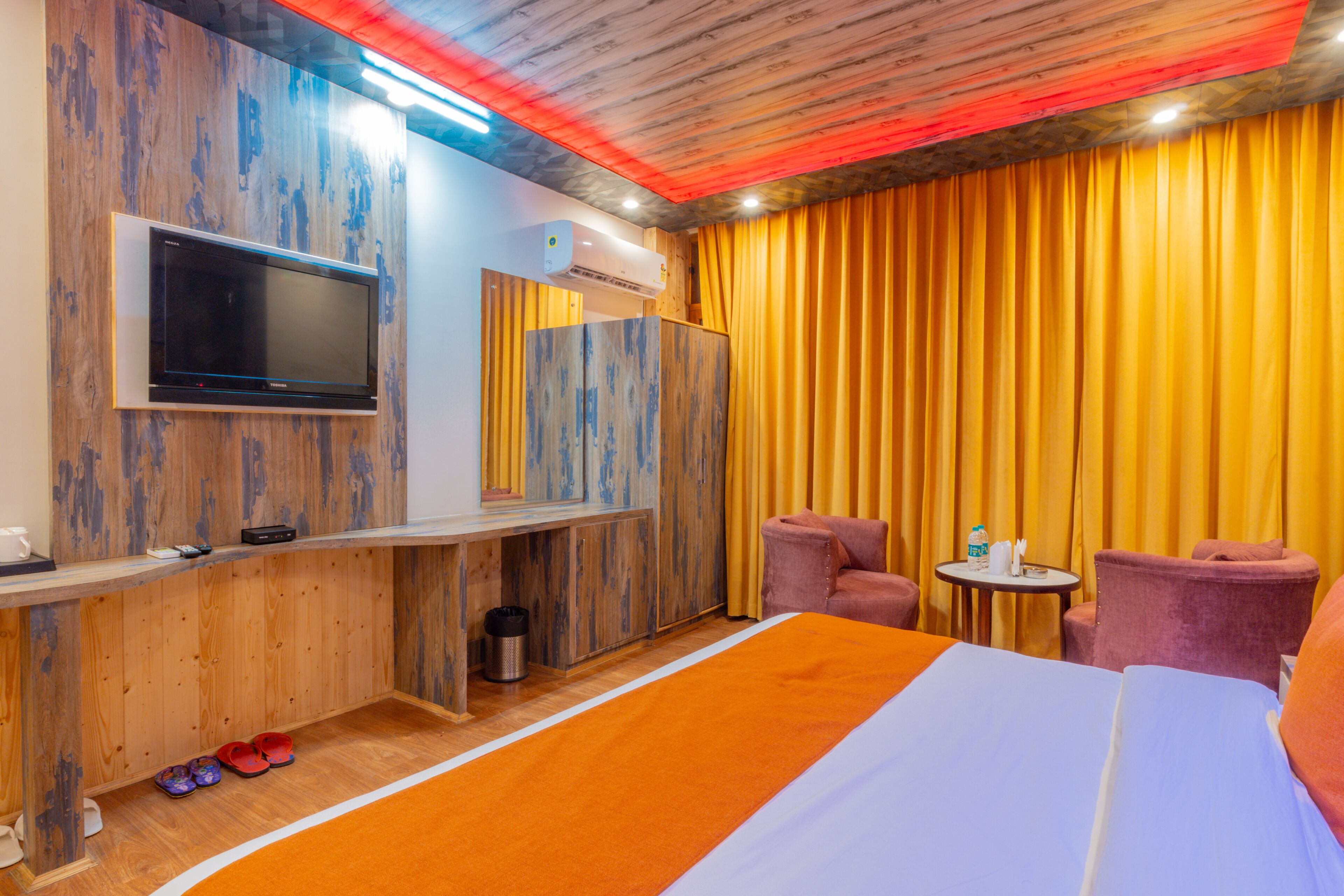 Ein Hotelzimmer mit Bett, Wandfernseher, Schreibtisch und zwei Stühlen.