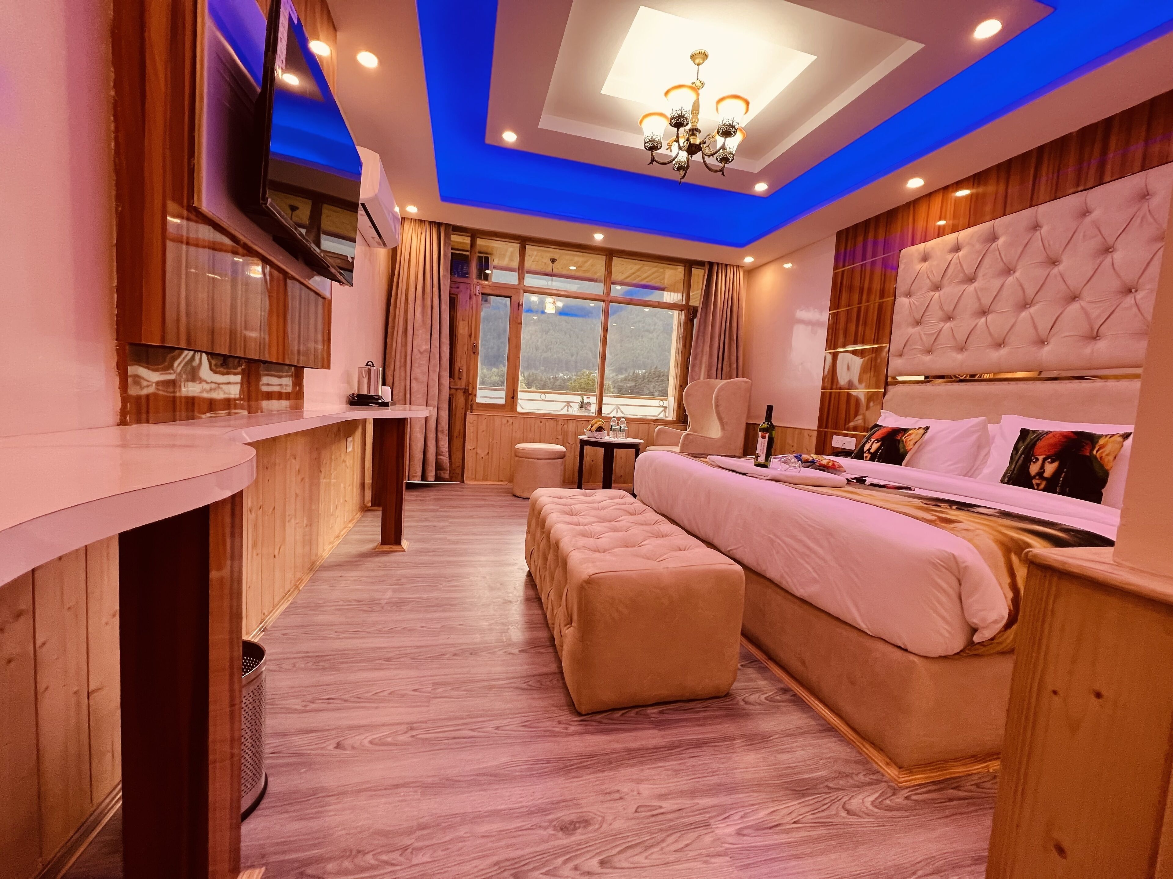 A modern bedroom with a large bed, a small desk, and a view of the outdoors.