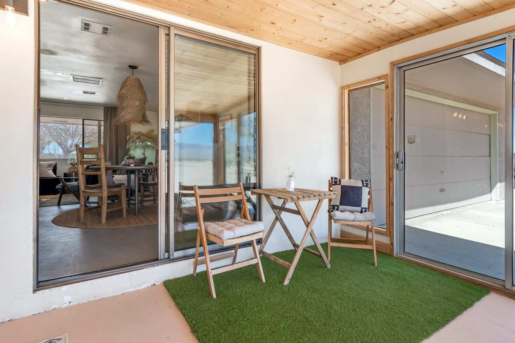 Una habitación con puerta de vidrio que da a un balcón con césped artificial, mobiliario de madera y vistas al exterior.