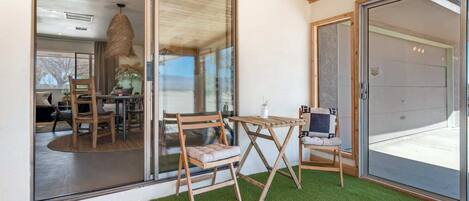 Una habitación con puerta de vidrio que da a un balcón con césped artificial, mobiliario de madera y vistas al exterior.