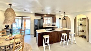 A modern kitchen with a central island, bar stools, and pendant lighting. - The Castle House: Hideaway w Cowboy Pool (Joshua Tree)