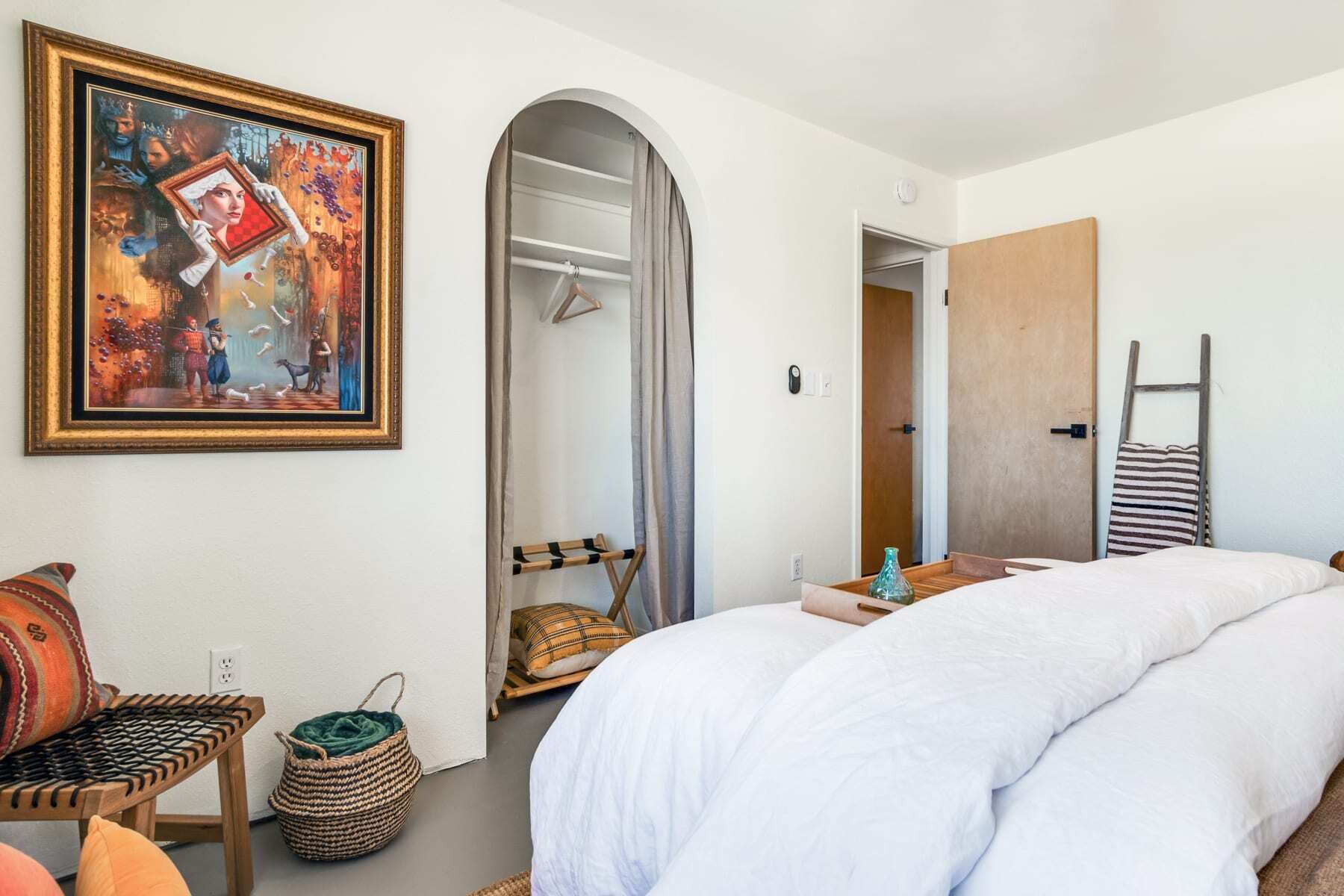 A bedroom with a bed, a wardrobe, a painting, and a door leading to another room.