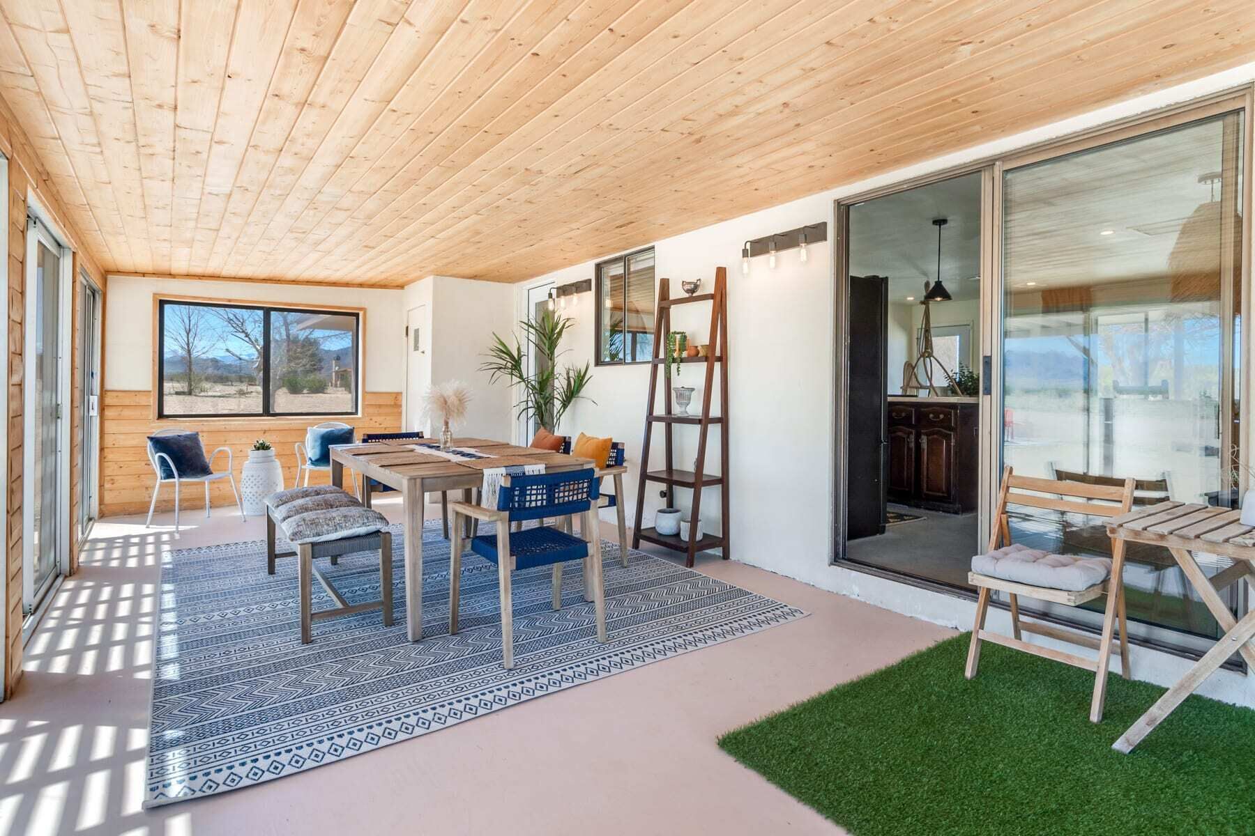 A modern interior with a wooden ceiling, a dining area with blue chairs, a large window, and a view of the outdoors.