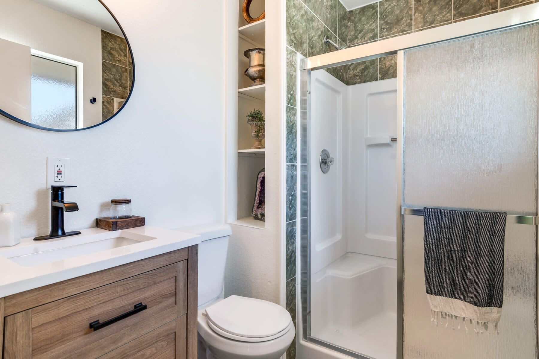 A modern bathroom with a toilet, a sink with a faucet, a mirror, and a shower area with a towel hanging on the door.
