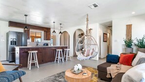 A modern kitchen with a central island, bar stools, and a hanging chair. - The Castle House: Hideaway w Cowboy Pool (Joshua Tree)