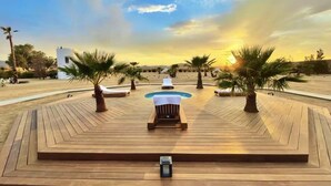 A wooden deck with a pool, palm trees, and lounge chairs. - The Castle House: Hideaway w Cowboy Pool (Joshua Tree)