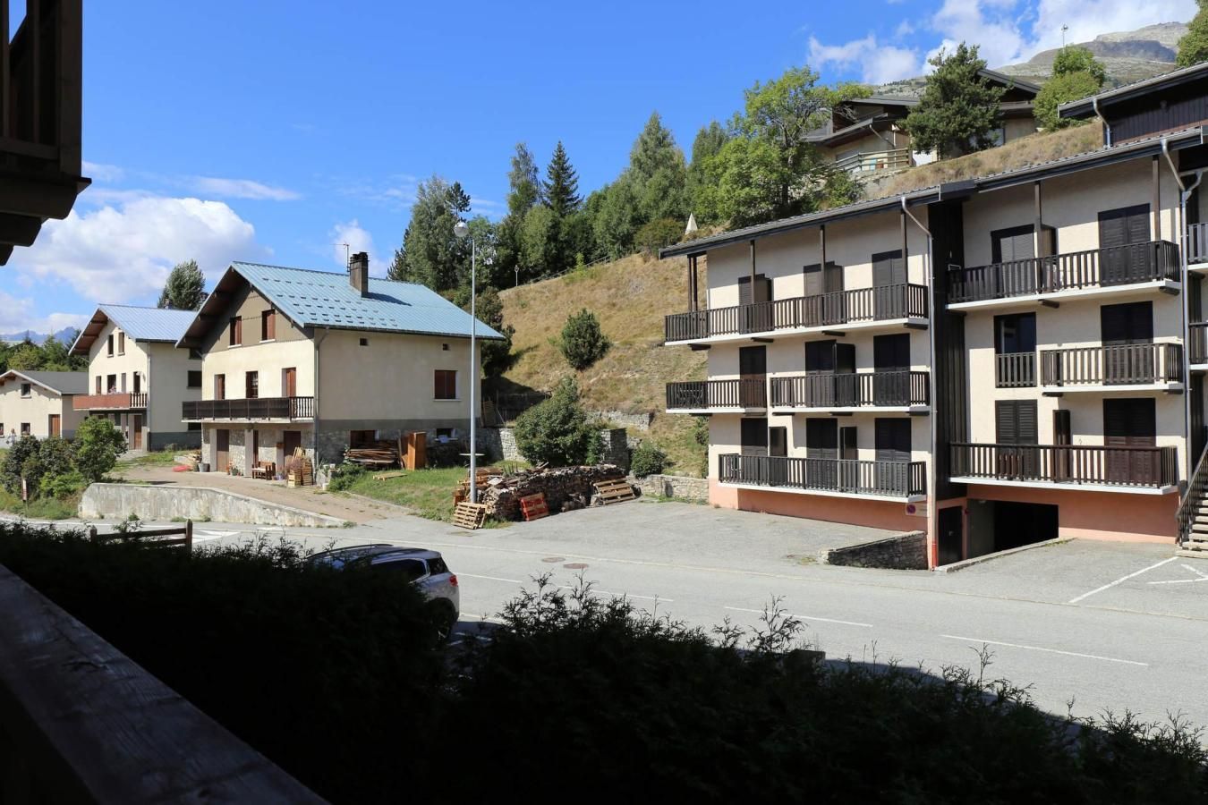 A multi-story building with balconies, a parking area, and a mountainous backdrop.