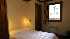 Ein Einzelbett mit weißer Decke in einem Zimmer mit Fenster, Heizkörper und Tür.