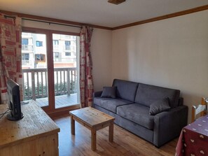 Un salon avec un canapé gris, une table basse en bois et un téléviseur posé sur un meuble en bois.