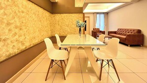 A modern dining area with a glass table and white chairs, a brown sofa, and a textured wall.