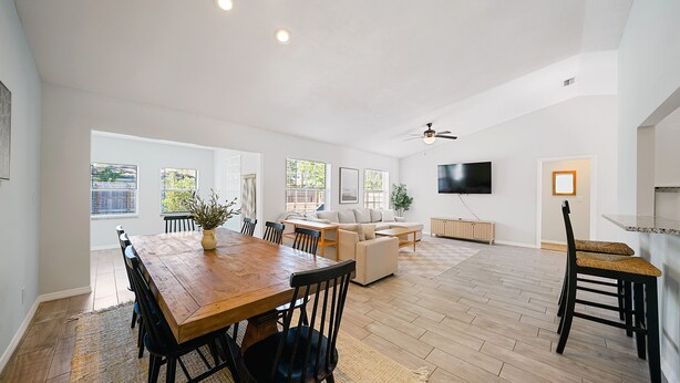 A spacious living area with a wooden dining table, sofas, and a TV mounted on the wall.