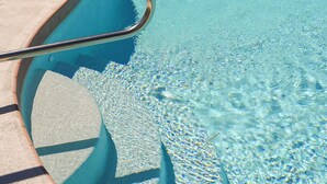 A swimming pool with clear water, a metal ladder, and a wooden fence in the background.