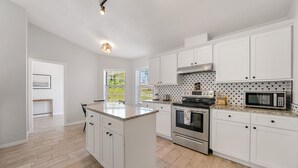 A modern kitchen with white cabinets, a granite countertop, stainless steel appliances, and a view of the outdoors through the windows.