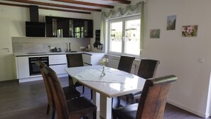 Una cocina moderna con armarios blancos, horno integrado y comedor con mesa blanca y cuatro sillas.