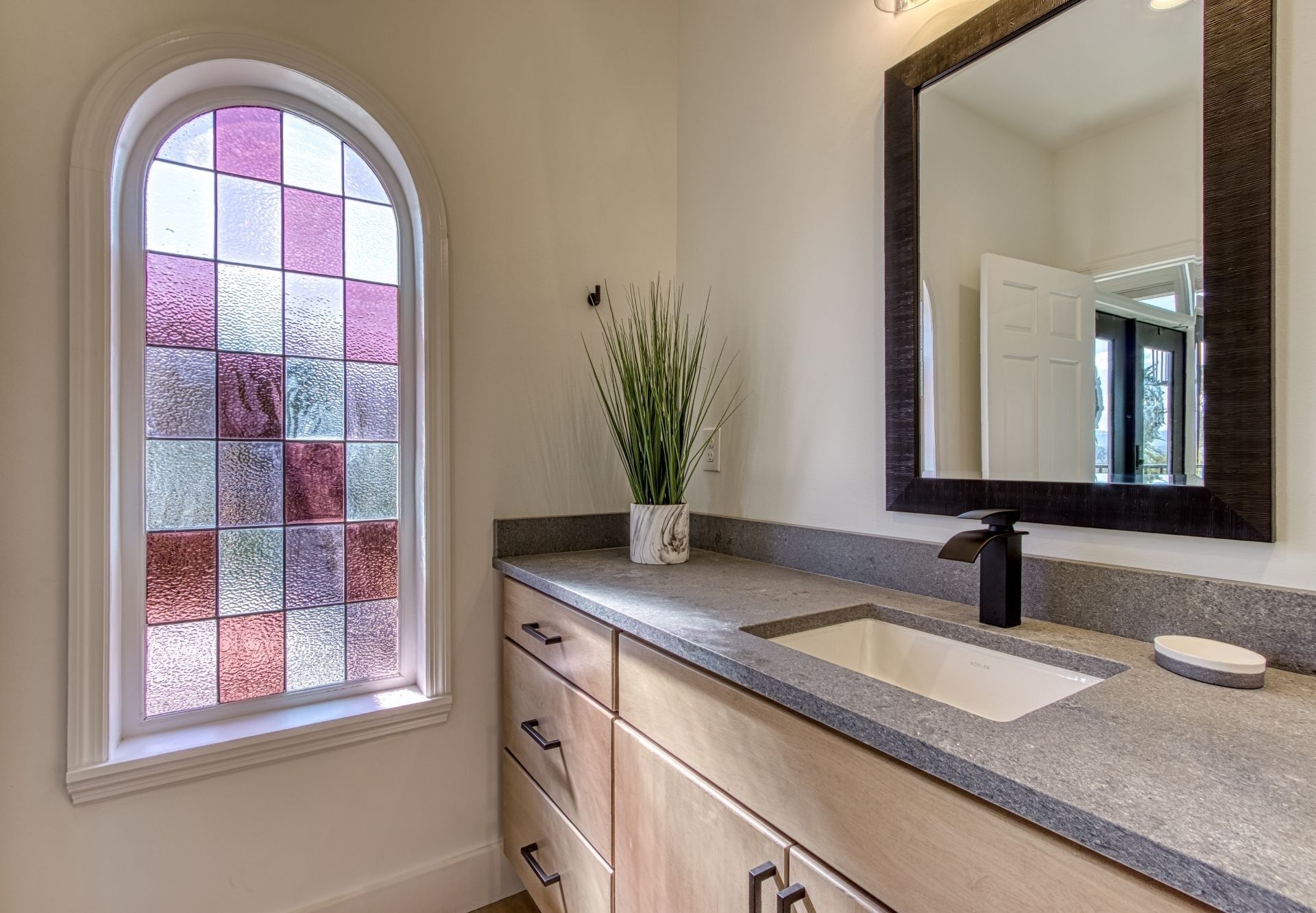 A bathroom with a vanity, a sink, a mirror, and a window with stained glass.