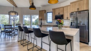 Cozinha moderna com armários de madeira, geladeira de aço inoxidável e uma ilha central com banquetas.