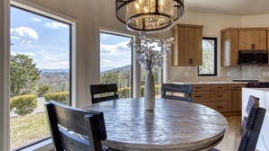 Uma sala de jantar com mesa redonda, cadeiras, um vaso com flores e vista para o exterior.
