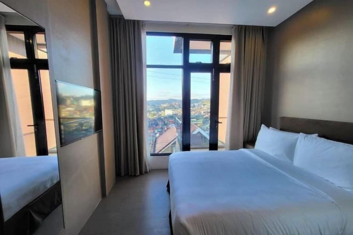 A hotel room with two beds, a TV, and a large window with a city view.