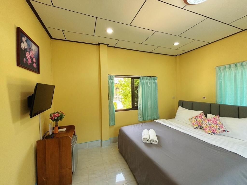 A hotel room with a bed, a desk with a TV, a window with curtains, and a picture on the wall.