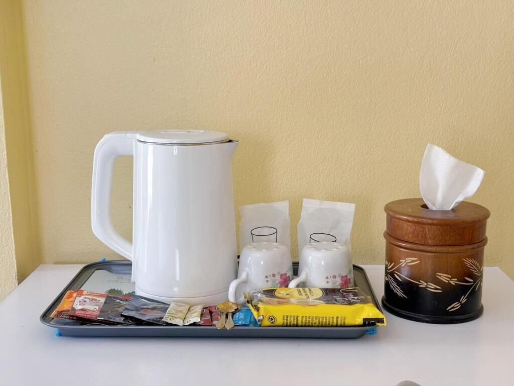 Una bandeja con una cafetera blanca, dos teteras, una caja de pañuelos y algunos aperitivos envasados.