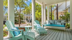 Une véranda abritée avec deux fauteuils Adirondack, une balançoire et une petite table.